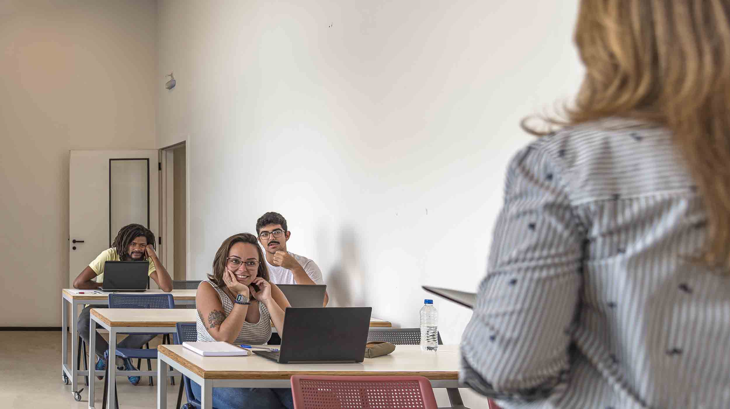 Brazilian university students in the classroom sitting in a row of desks, with a teacher, during content explanation