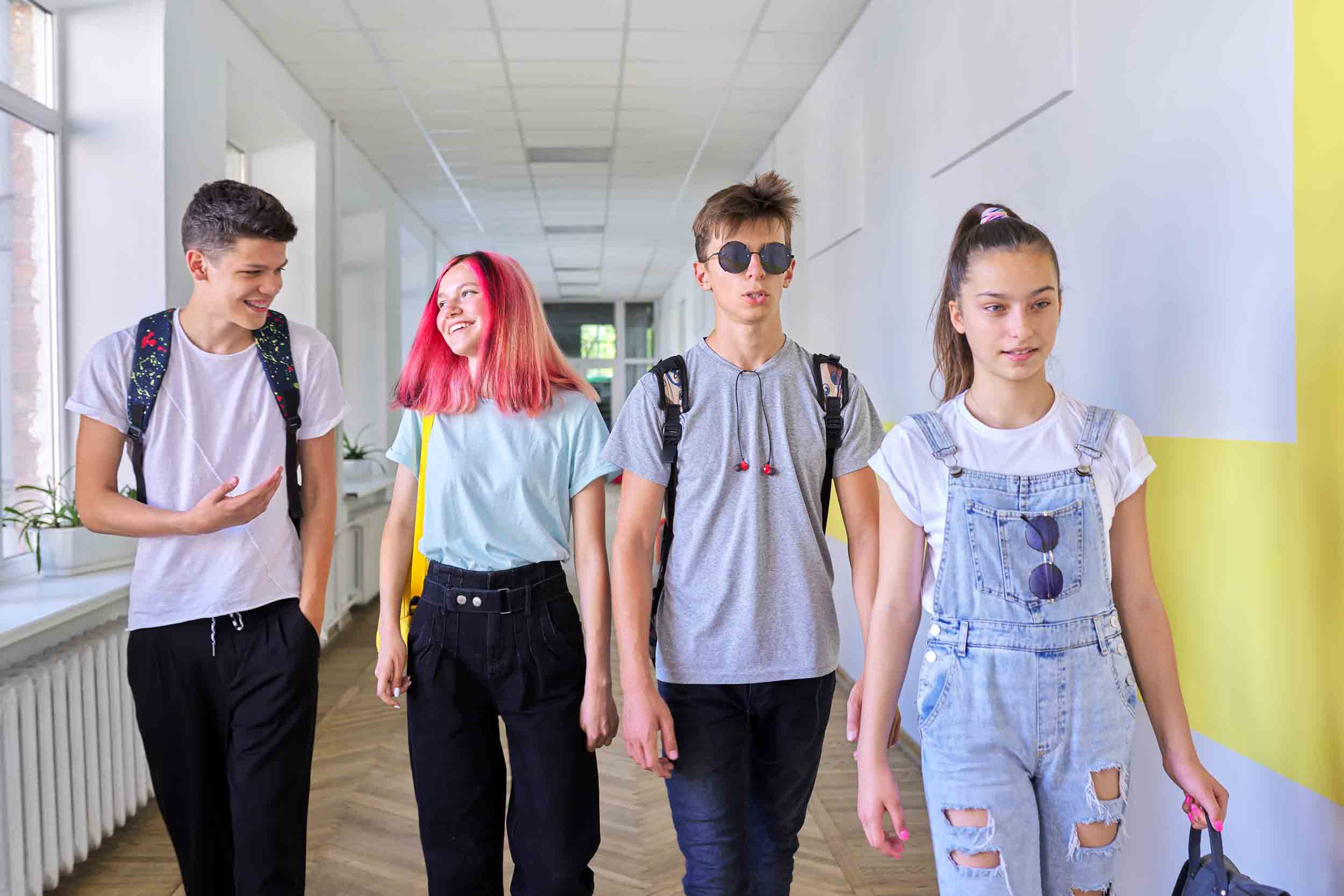 Group of teenage students walking together along school corridor, schoolchildren smiling and talking. Education, high school, adolescence concept